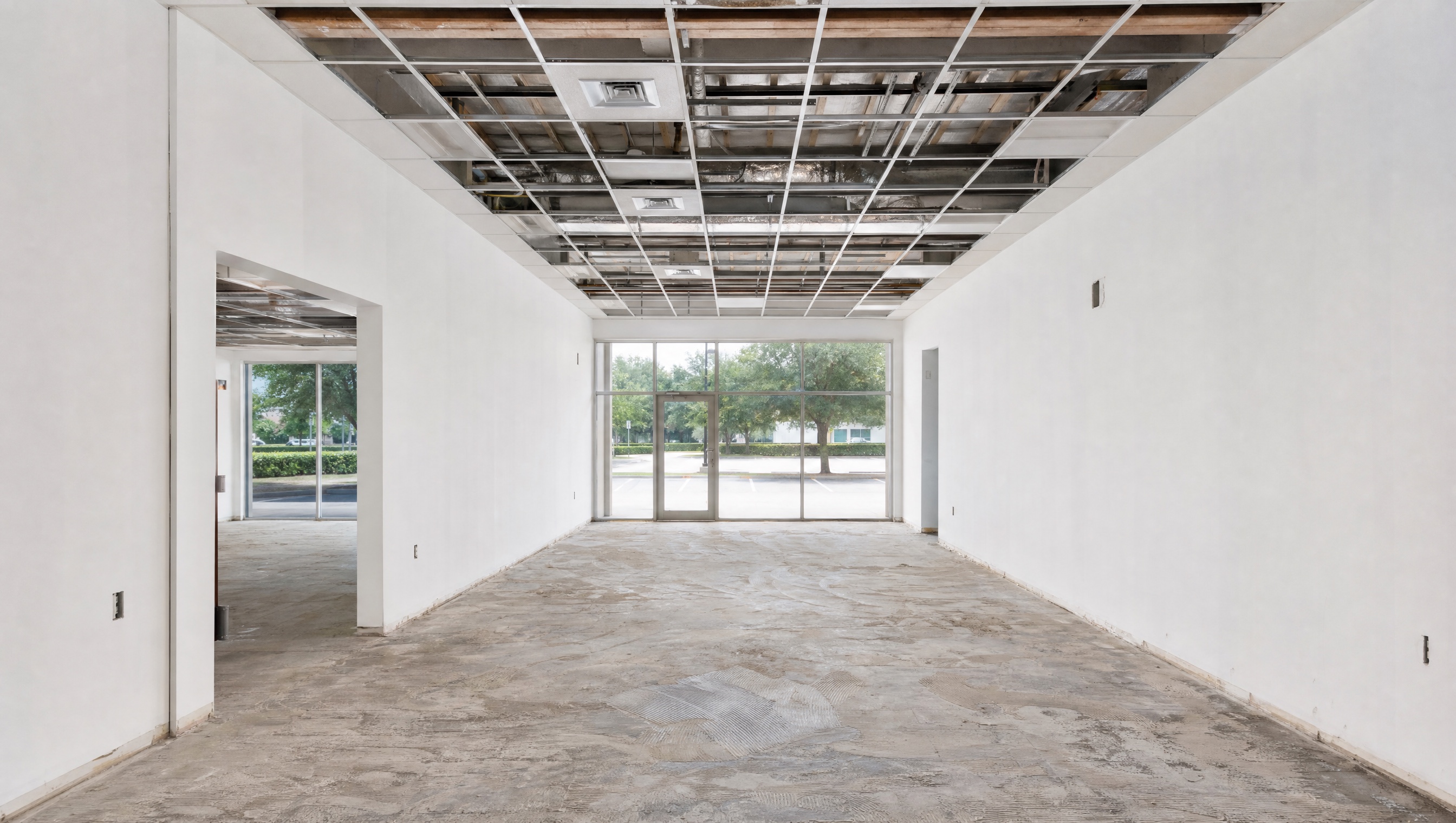 A vacant second-generation restaurant space stripped back to the slab: ceiling grid open, storefront glazing intact, dining room empty.
